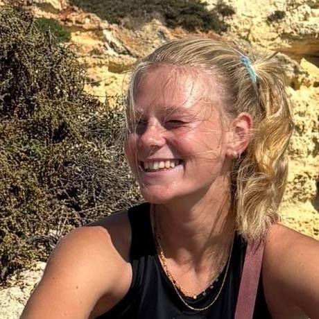 Mia, Gründerin von Peraly, lachend auf einem Felsen an der Küste